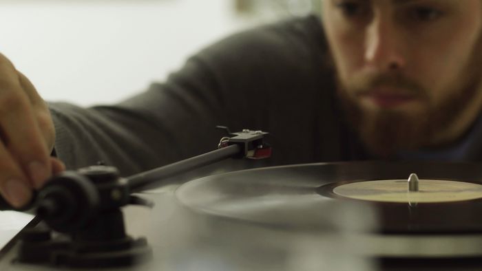 A close up shot of a man placing the needle of a record player down onto an album.